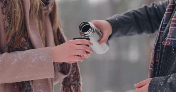 A loving couple man and woman in the winter forest drinking tea from a thermos. Stylish man and woman in a coat in the Park in winter for a walk. Slow motion — Stock Video