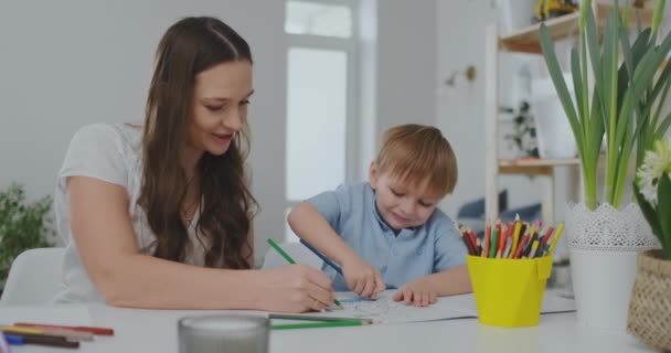 İki çocuk bir aile ve masada oturan genç bir anne renkli kalemler ile kağıt çekiyor. Çocuklarda yaratıcılığın geliştirilmesi. — Stok video
