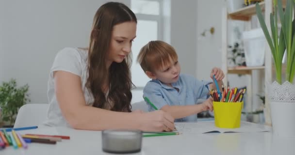 Une famille de deux enfants et une jeune mère assise à la table dessinent sur du papier avec des crayons de couleur. Développement de la créativité chez les enfants. intérieur blanc propre — Video