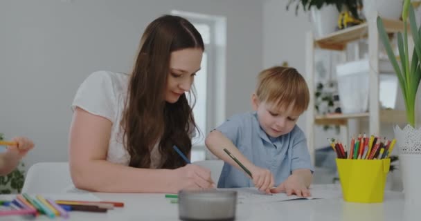 İki çocuk bir aile ve masada oturan genç bir anne renkli kalemler ile kağıt çekiyor. Çocuklarda yaratıcılığın geliştirilmesi. — Stok video