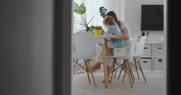 Mladá matka se dvěma dětmi, které sedí u bílého stolu, při pomalém pohybu kreslí barevné tužky. — Stock video