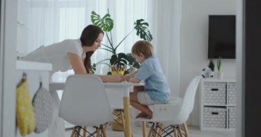 Mutfak ışık üzerinde oturan iki çocuk okul-görevler için kalem çizimleri çizin. Anne Çocuk ve gülümsüyor mutfakta bakar