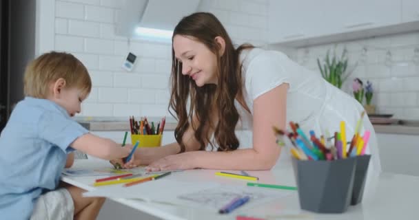 Giovane bella mamma e figlio disegnare con matite colorate seduti a tavola in cucina — Video Stock