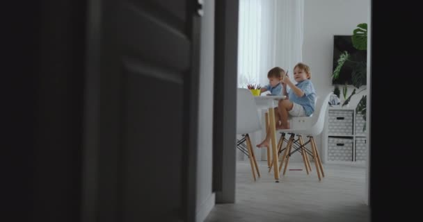 Família feliz jovem mãe bonita e dois filhos desenhar com lápis de cor sentado à mesa na cozinha. A câmera se move em câmera lenta — Vídeo de Stock