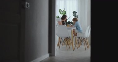 Genç güzel anne ve iki oğlu ile renkli kalemler mutfakta masada oturan çizin. Kamera ağır çekimde hareket eder.