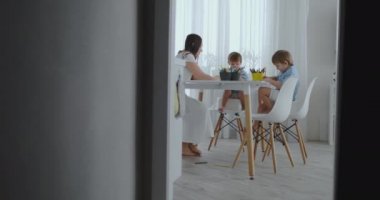 Mutlu aile genç güzel anne ve iki oğlu ile renkli kalemler mutfakta masada oturan çizin. Kamera ağır çekimde hareket eder.