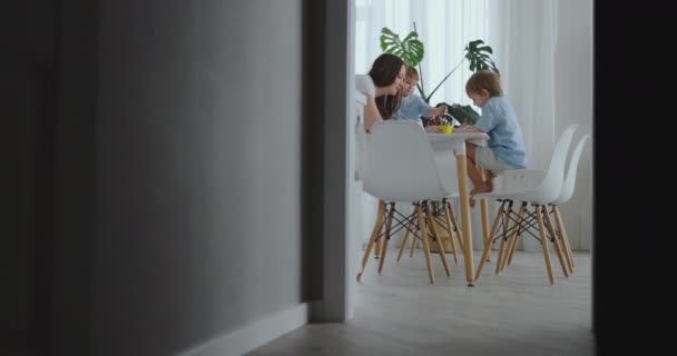 Moeder helpt zonen leren tekenen doen van huiswerk preschool voorbereiding thuis zitten in de witte keuken. Twee broers trekken samen een portret van de moeder — Stockvideo