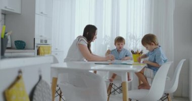 Anne yardımcı olur öğrenmek çizmek oğulları eve beyaz mutfakta oturmuş, ev ödevi okul öncesi hazırlık yapıyor.
