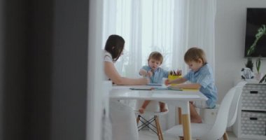 Çocuklardan iki çocuk annesi mutfakta oturuyor ile çizin. Mutlu aile evde.