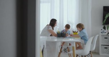 Anne yardımcı olur öğrenmek çizmek oğulları eve beyaz mutfakta oturmuş, ev ödevi okul öncesi hazırlık yapıyor. İki çocuk kardeşler birlikte anne bir portresini çizmek