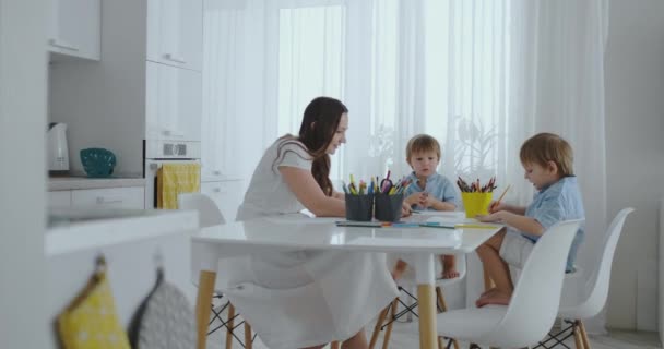 Due figli di ragazzi disegnano con sua madre seduta in cucina . — Video Stock