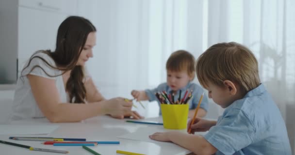 Dvě děti chlapců kreslit s jeho matkou, sedí v kuchyni. Šťastná rodina doma. — Stock video