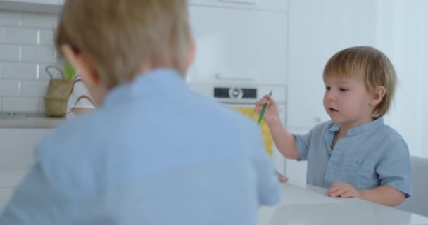 Dos hijos de niños dibujan con su madre sentada en la cocina . — Vídeo de stock