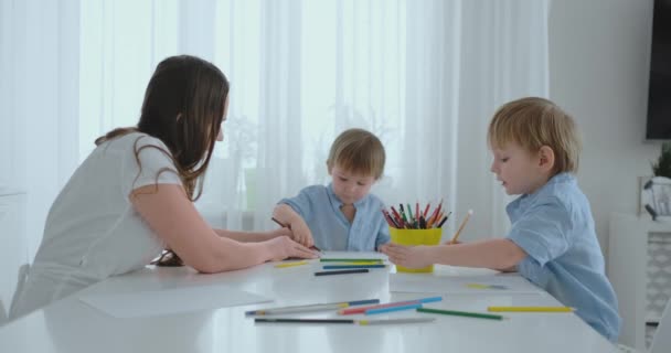 Mamma e i suoi due figli seduti al tavolo della cucina disegno matite colorate famiglia disegno sul prato in estate . — Video Stock