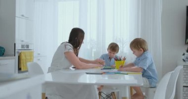 Annem ve onun iki oğlu renkli kalemler aile çimenlerin üzerine yaz aylarında çizim mutfak masasında oturuyor. Çocuklar öğrenmek çizmek ve anne çizim ile yardımcı olur.