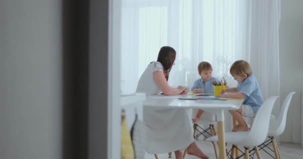 Moeder en haar twee zoons zittend aan de keukentafel kleurpotloden familie tekening puttend uit het gazon in de zomer. — Stockvideo