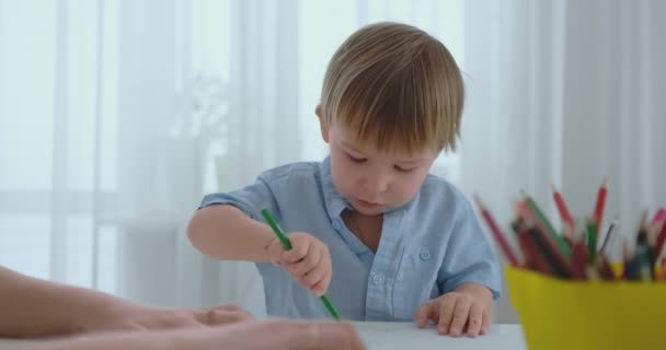 Мальчик рисует карандашный рисунок счастливой семьи, сидящей за столом — стоковое видео