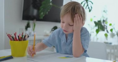 Mutfakta masada oturan mavi tişört bir çocukta ev ödevi okul öncesi eğitim yaparken bir kalem çizer