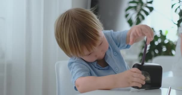Мальчик точит карандаш, сидя за столом — стоковое видео