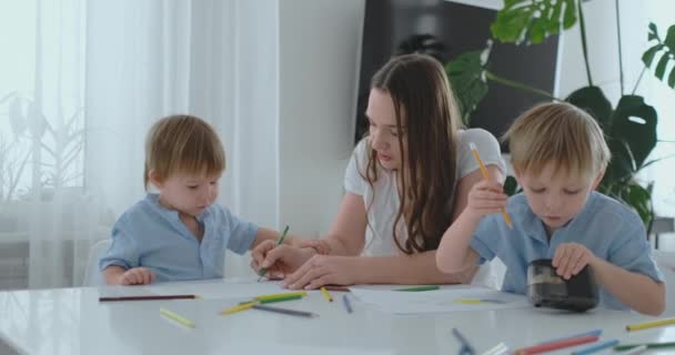 Mladá maminka a dva syny 2-4 let čerpat tužky na boomega sedí u stolu obývacího pokoje v pomalém pohybu — Stock video