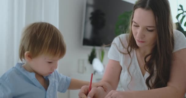 Mamma hjälper två söner 2 och 4 år gamla att göra förskola läxor för att rita en bild med pennor — Stockvideo