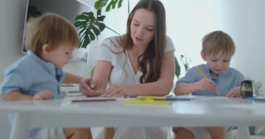 Anne iki oğlu 2 ve 4 yaşında bir resim çizmek ile kalemler için okul öncesi ödev yapmak için yardımcı olur.