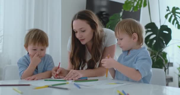 Молодая мама и два сына 2-4 лет рисовать карандаши рисовать на Бумега сидя за столом гостиной в замедленной съемке — стоковое видео