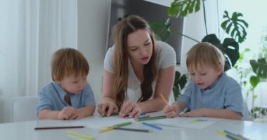 Anne iki oğlu 2 ve 4 yaşında bir resim çizmek ile kalemler için okul öncesi ödev yapmak için yardımcı olur.