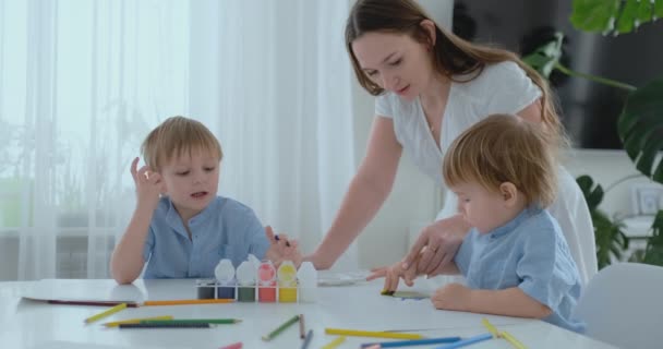 Annem onun oğulları yaratıcı becerilerini geliştirmeye yardımcı olur ve onlarla çizim boyalar parmak yardımıyla oluşturmak için devreye girer. Çocuk gelişimi. Yaratıcı aile. Sevgi dolu anne — Stok video