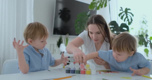 La familia se divierte pintando sobre papel con los dedos pintados. Mamá y dos niños pintan con los dedos sobre papel — Vídeos de Stock