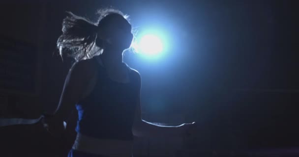 Тренування дівчини-винищувача стрибає мотузкою в темній кімнаті світла від ліхтаря — стокове відео