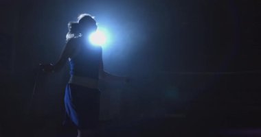 Genç güzel kadın profesyonel bir boksör eğitim salonunda karanlık bir odada ışık contra bir ip atlar. Soğuk ışık