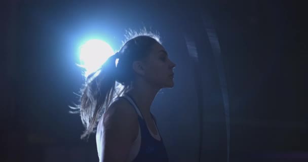Cardio training for fighters. Young beautiful woman professional boxer in training in the hall jumps on a rope in the light of the contra in a dark room in blue clothes — Stock Video