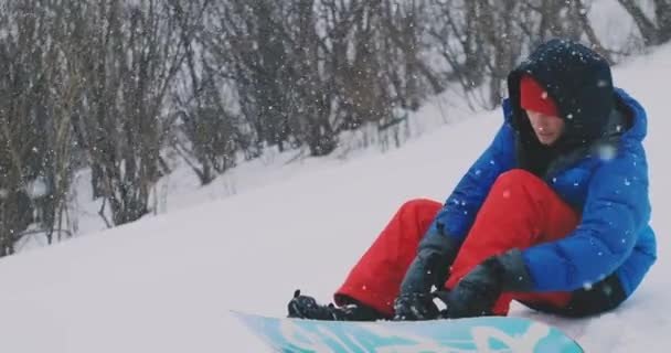 Mannen sitter i snö dragkedjan stövlar snowboard — Stockvideo