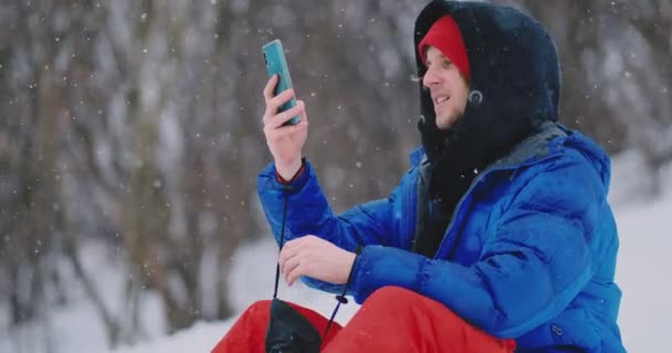 Mužské snowboardista sedět na sněhu, pořizování fotografií v telefonu nádherné scenérii letoviska pro sociální sítě — Stock video