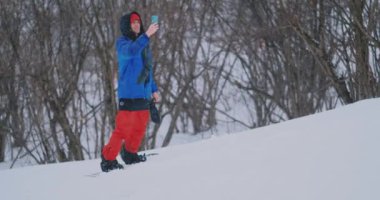 Yavaş çekim bir kayak pisti üzerinde sürüş sırasında bir smartphone kullanarak bir snowboarder