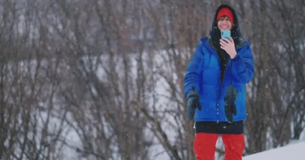 Fotografía en cámara lenta de un snowboarder usando un smartphone mientras conduce en una pista de esquí — Vídeos de Stock
