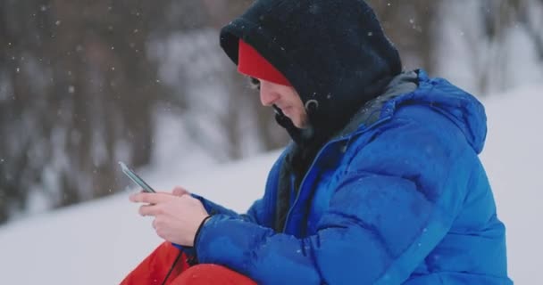 Homem snowboarder sentado na neve tirando fotos no telefone belas paisagens do resort para redes sociais — Vídeo de Stock