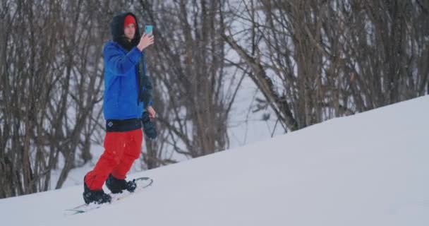 Utilice su teléfono inteligente para tomar fotos de paisajes mientras hace snowboard en la pista de esquí — Vídeo de stock