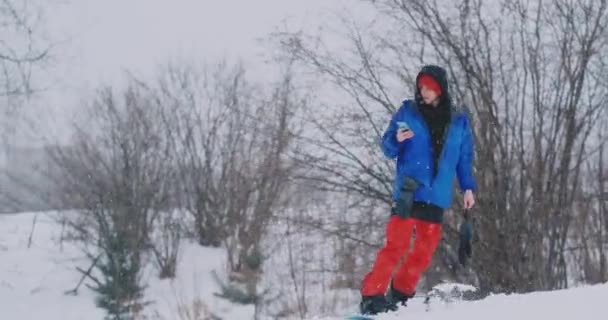 Snowboarder męski jeździ Zarząd narciarskiego stoku snow oraz pisania wiadomości do smartfona do znajomych — Wideo stockowe