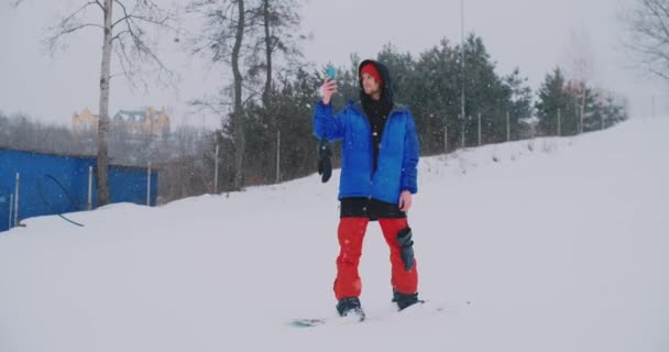 Yavaş çekim bir kayak pisti üzerinde sürüş sırasında bir smartphone kullanarak bir snowboarder — Stok video