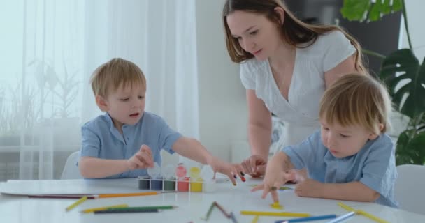 The family has fun painting on paper with their fingers in paint. Mom and two children paint with fingers on paper — Stock Video