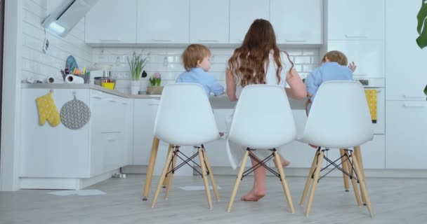 Rear view, back. Two children of boys and mother are engaged in creative development doing homework by fingering on paper. The development of tactile sensations and small mathematics. — Stock Video
