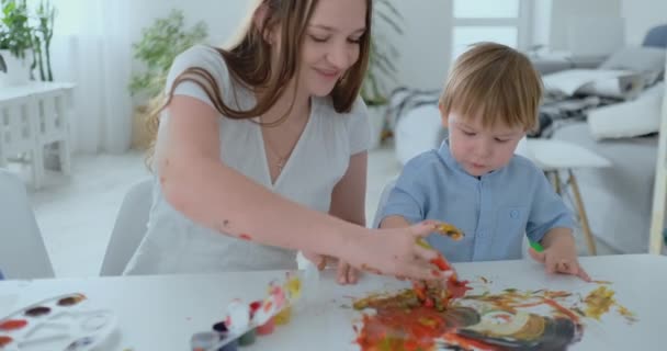 Mutter hilft ihrem Sohn, mit Farbe einen Handabdruck auf Papier zu machen. gemeinsame Freizeitangelegenheit des Kindes. glückliche und fürsorgliche Mutter — Stockvideo