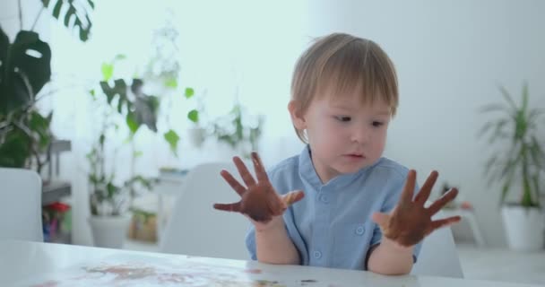 Το αγόρι αφήνει handprints σε χαρτί με τη βοήθεια του ένα τράνταγμα. Αντλώντας τα δάχτυλα με pomuschiyu χρώματα. Ανάπτυξη των δημιουργικών ικανοτήτων σε παιδιά — Αρχείο Βίντεο