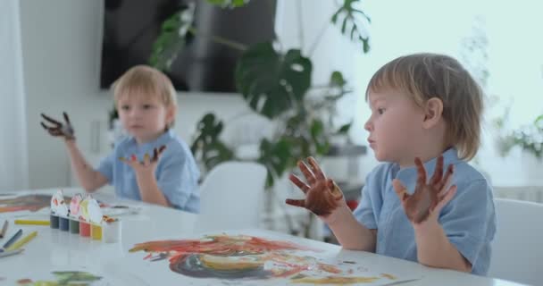 Criança com as mãos pintadas em tintas coloridas prontas para impressões manuais — Vídeo de Stock