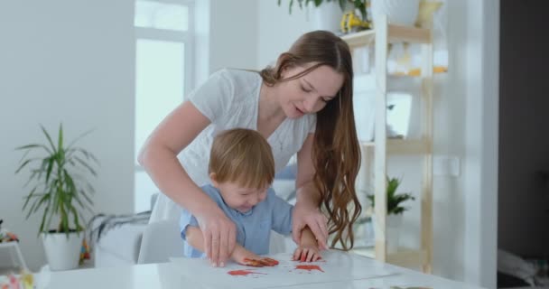 Mom helps her son to make a handprint on paper using paint. Joint leisure matter of the child. Happy and caring mom — Stock Video
