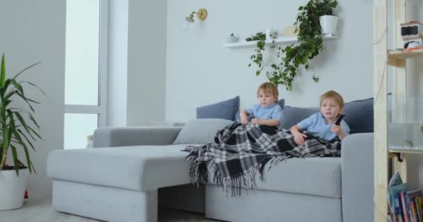 Due ragazzi, 4 e 2 anni, stanno guardando la TV seduti sul divano. Un eccitante programma televisivo. Guarda i cartoni animati. I bambini guardano un emozionante programma televisivo . — Video Stock