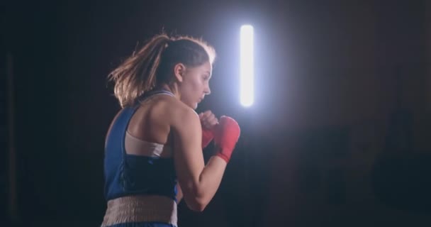 女拳击手在黑暗的房间训练与背光在慢动作侧视图。稳定射门 — 图库视频影像