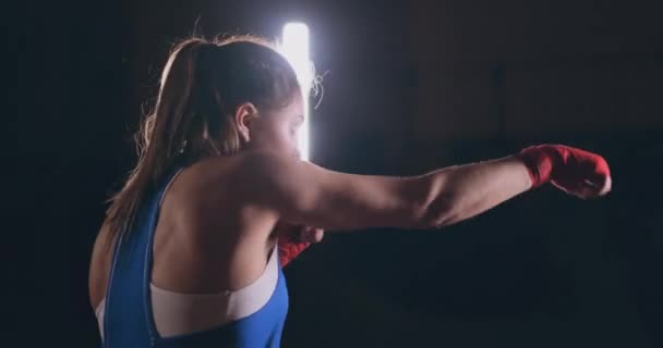 Entrenamiento de boxeadora femenina en habitación oscura con contraluz en cámara lenta. steadicam tiro — Vídeos de Stock